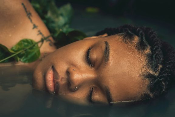 Beautiful woman with braids lying face-down with eyes closed, in a peaceful spa setting.